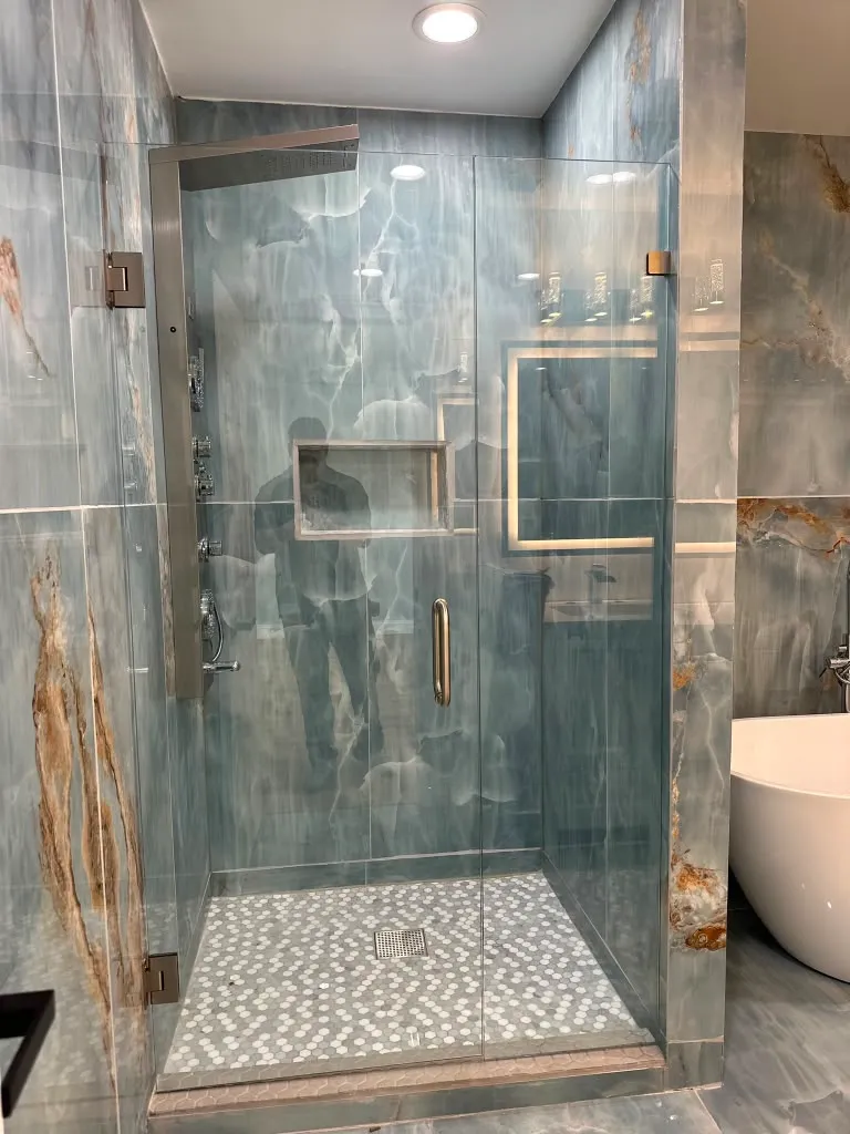 Cabina de ducha sin marco sobre piedra azul-gris dramatica con herrajes dorados